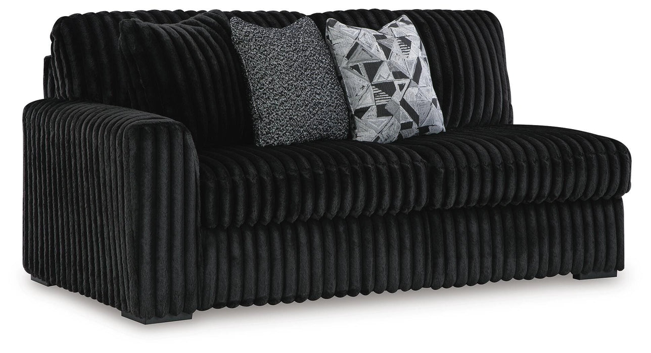 Black ribbed fabric loveseat with two throw pillows. One pillow is gray textured, the other is black and white with a geometric pattern.