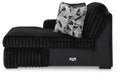 Black faux fur chaise lounge with a ribbed texture, featuring a high right armrest and back. It includes a decorative throw pillow with a black, white, and gray geometric pattern. The base is smooth black with a silver-toned accent.
