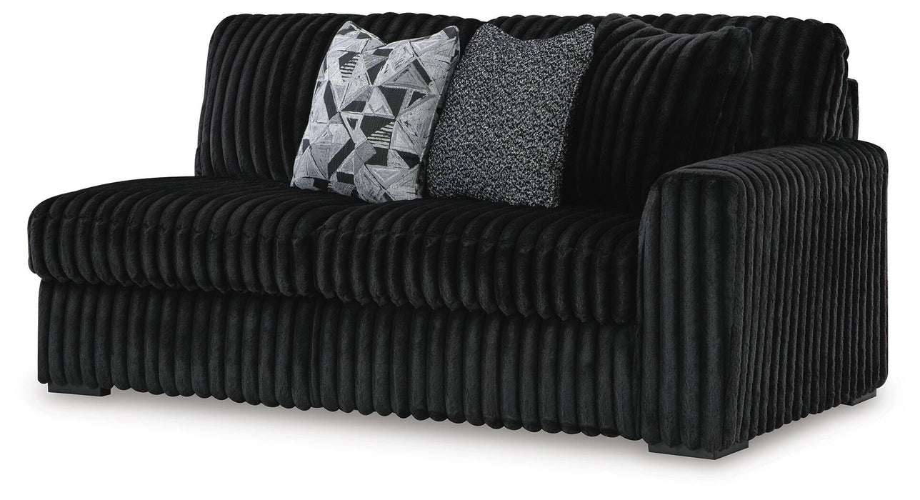 Black channeled plush fabric loveseat with two decorative throw pillows. One pillow features a black and white geometric pattern, the other is a textured gray and black knit.