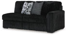 Black channeled plush fabric loveseat with two decorative throw pillows. One pillow features a black and white geometric pattern, the other is a textured gray and black knit.