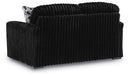 Black channel-tufted loveseat with a plush, ribbed velvet texture. It includes a black and white geometric patterned throw pillow and rests on small dark block feet.