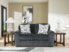 Dark gray ribbed corduroy-style sofa with two geometric gray and white throw pillows, flanked by dark wood end tables with white textured lamps, in a modern living room with light paneled walls, abstract art, and a gray and white rug.