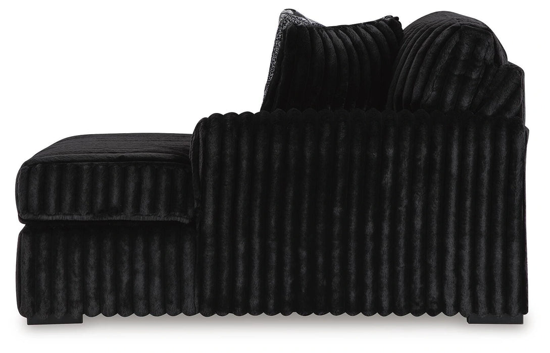 Black plush fabric armless sofa or sectional piece with a ribbed texture on the base and back cushions. The bottom edge features a scalloped trim, and the back cushions are soft and rounded.