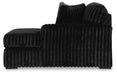 Black plush fabric armless sofa or sectional piece with a ribbed texture on the base and back cushions. The bottom edge features a scalloped trim, and the back cushions are soft and rounded.
