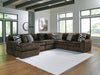 Large brown U-shaped sectional sofa with ribbed fabric texture and plush cushions, accented with patterned and solid grey throw pillows, in a modern living room with hardwood floors and a white textured rug.