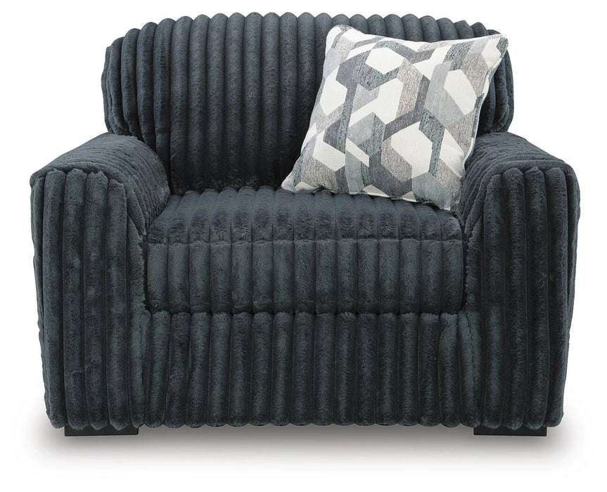 Dark gray armchair with a plush, ribbed chenille-like fabric, featuring wide, rounded arms and a high back. A decorative throw pillow with a gray and white geometric pattern rests on the seat.