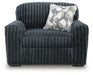 Dark gray armchair with a plush, ribbed chenille-like fabric, featuring wide, rounded arms and a high back. A decorative throw pillow with a gray and white geometric pattern rests on the seat.