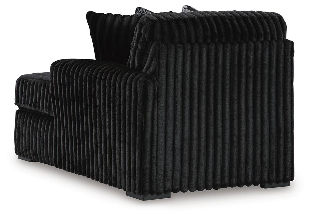 Black armless chair with plush, vertically ribbed upholstery. The back and side panels feature prominent vertical channels, and it rests on dark, low-profile block feet.