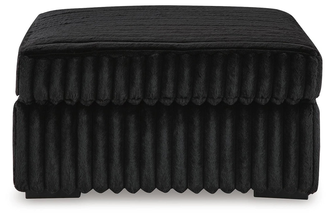 Black rectangular storage ottoman with a plush, vertically ribbed fabric texture on the sides and a slightly textured top cushion, resting on small dark feet.