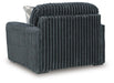 Dark gray armchair upholstered in a deeply ribbed, plush fabric, featuring a wide back and arms, and sitting on dark block feet. A small plaid pillow is visible behind the back cushion.
