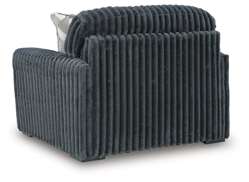 Dark gray armchair upholstered in a deeply ribbed, plush fabric, featuring a wide back and arms, and sitting on dark block feet. A small plaid pillow is visible behind the back cushion.