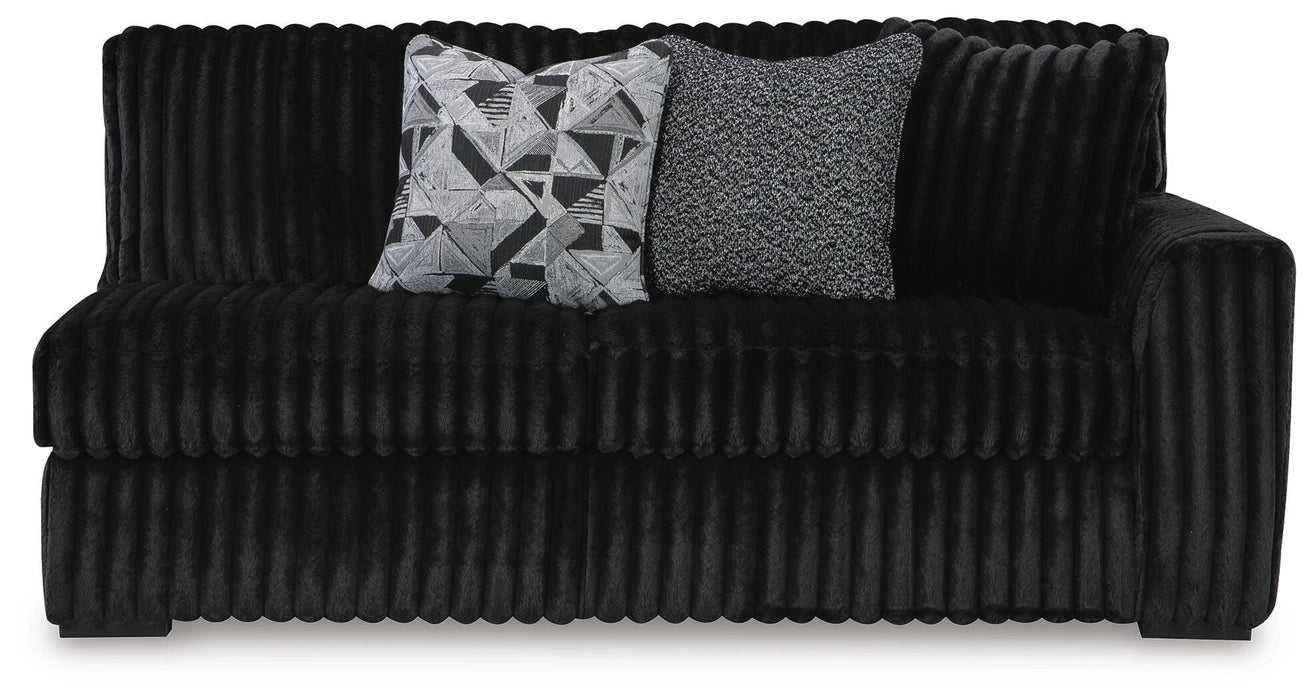 Black channeled plush sofa with two decorative pillows: one geometric black and white, one textured gray.