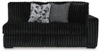 Black channeled plush sofa with two decorative pillows: one geometric black and white, one textured gray.