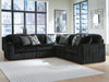 Dark gray L-shaped sectional sofa upholstered in a ribbed corduroy fabric, featuring solid and geometric patterned throw pillows. It sits on a light wood floor with a textured light gray rug in a modern living room with large windows overlooking a city.