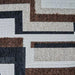 Close-up of a fabric swatch featuring a geometric pattern in brown, black, beige, and white. The pattern combines flat woven, shaggy, and quilted textures.