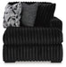 Oversized black ribbed plush armchair featuring three decorative pillows: one matching ribbed black, one black and white speckled, and one black and white geometric pattern.