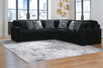 Black L-shaped sectional sofa with plush, vertically ribbed fabric, featuring solid textured gray and geometric patterned throw pillows. It sits on a light-colored abstract rug in a modern living room with large windows and gold wall decor.
