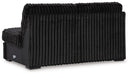 Black modular sofa section, shown from the rear three-quarter view. It is upholstered in a plush, vertically ribbed fabric that covers the back and visible side. The lower frame is smooth black, and it stands on dark, low-profile square feet.