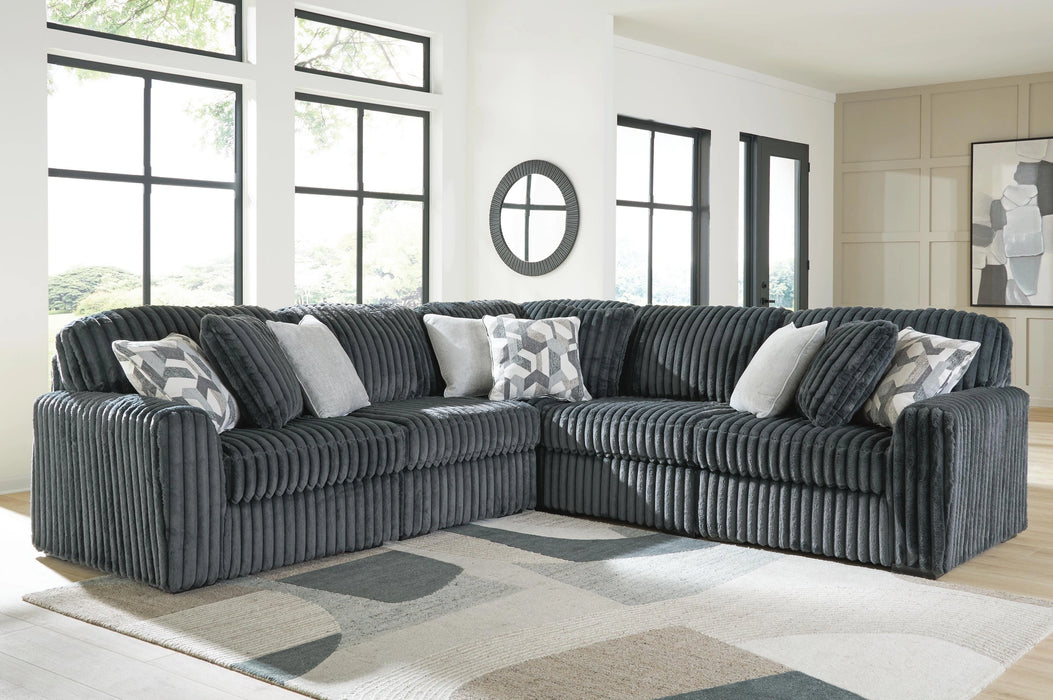Dark gray corduroy-textured sectional sofa with deep seats and plush cushions, adorned with light gray and geometric patterned throw pillows, in a bright modern living room with large windows and a geometric area rug.