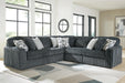 Dark gray corduroy-textured sectional sofa with deep seats and plush cushions, adorned with light gray and geometric patterned throw pillows, in a bright modern living room with large windows and a geometric area rug.