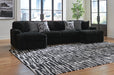 Black ribbed plush L-shaped sectional sofa with two decorative throw pillows (one speckled, one geometric) in a modern living room with hardwood floors, a black and white abstract rug, and large windows overlooking a city.
