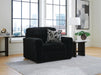 Black ribbed plush armchair with a geometric patterned throw pillow in a modern room with large windows overlooking a city, flanked by marble-top side tables.