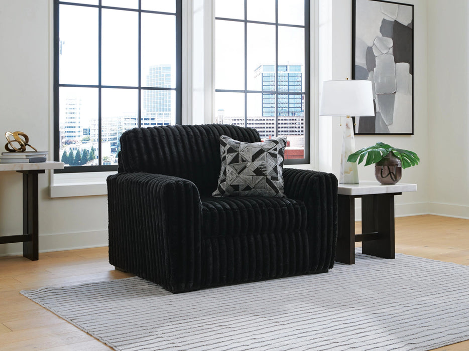 Black ribbed plush armchair with a geometric patterned throw pillow in a modern room with large windows overlooking a city, flanked by marble-top side tables.