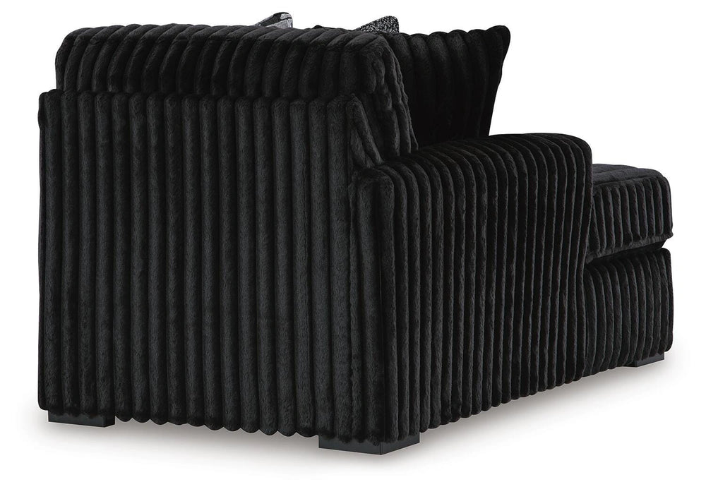 Black armchair upholstered in plush, vertically channeled fabric, with square arms and dark block feet, viewed from the back-side.