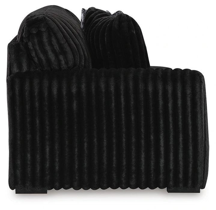 Black plush armchair with a deeply ribbed texture on the body and back cushions, featuring small dark feet, viewed from the side.