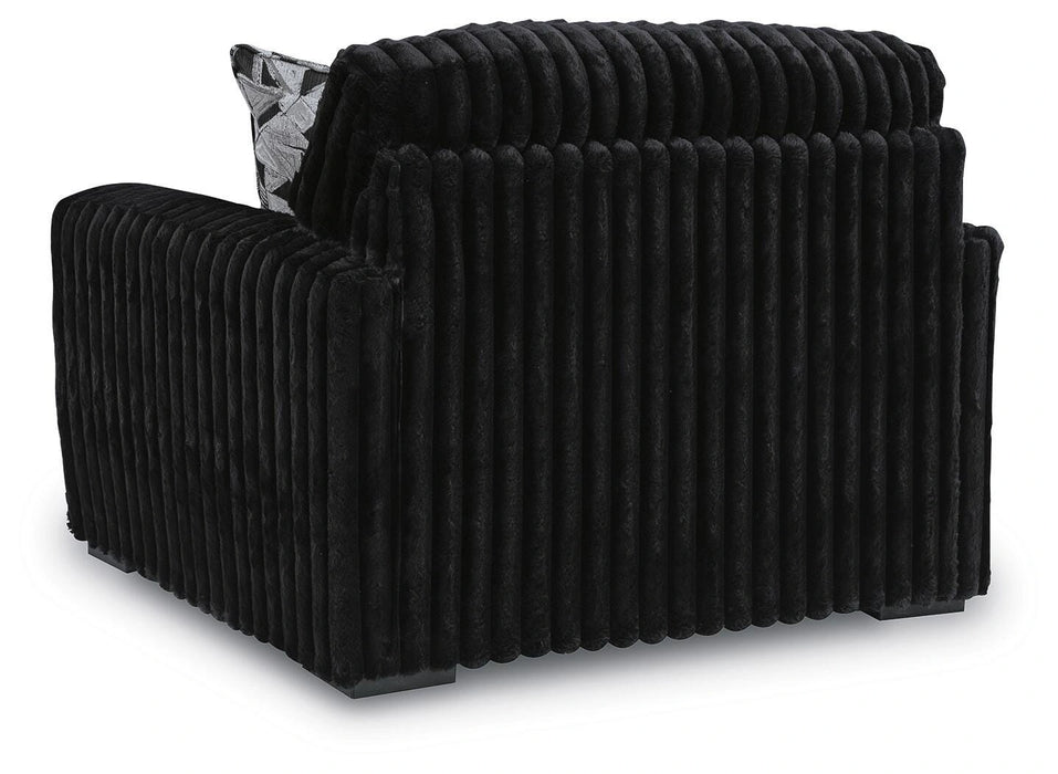 Black armchair with plush, vertically channeled fabric on the back and sides, and a patterned throw pillow visible.